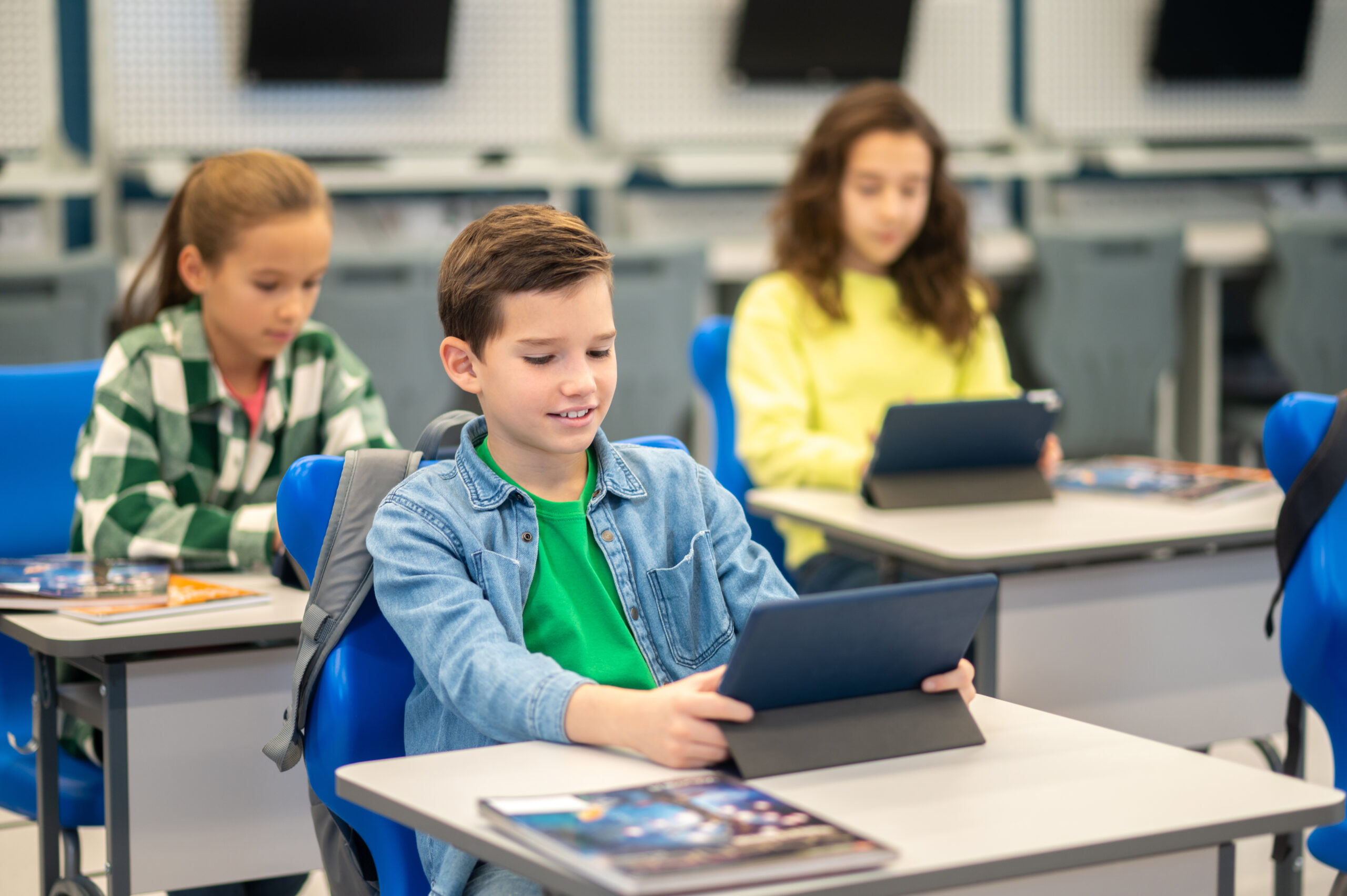 Lesson. Boy and girls sitting at desks carefully looking at their tablets studying at school